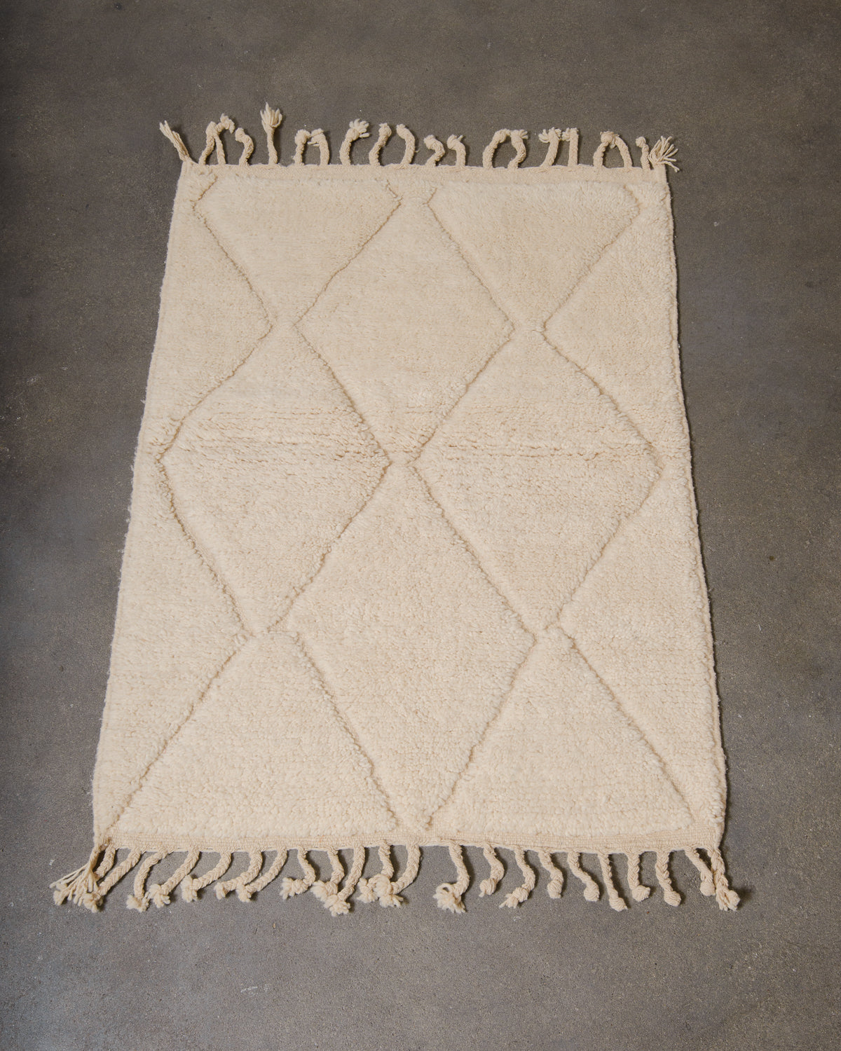 Beniourain rug in cream wool laying on concrete studio floor.